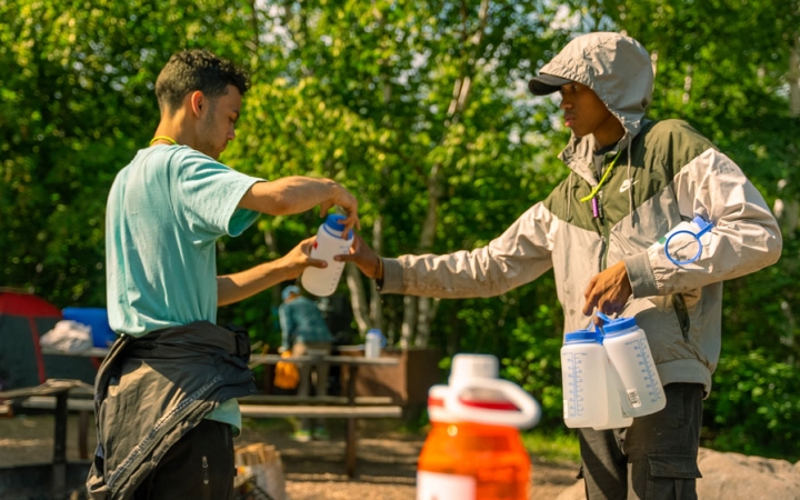 One person hands a water bottle to another while outdoors